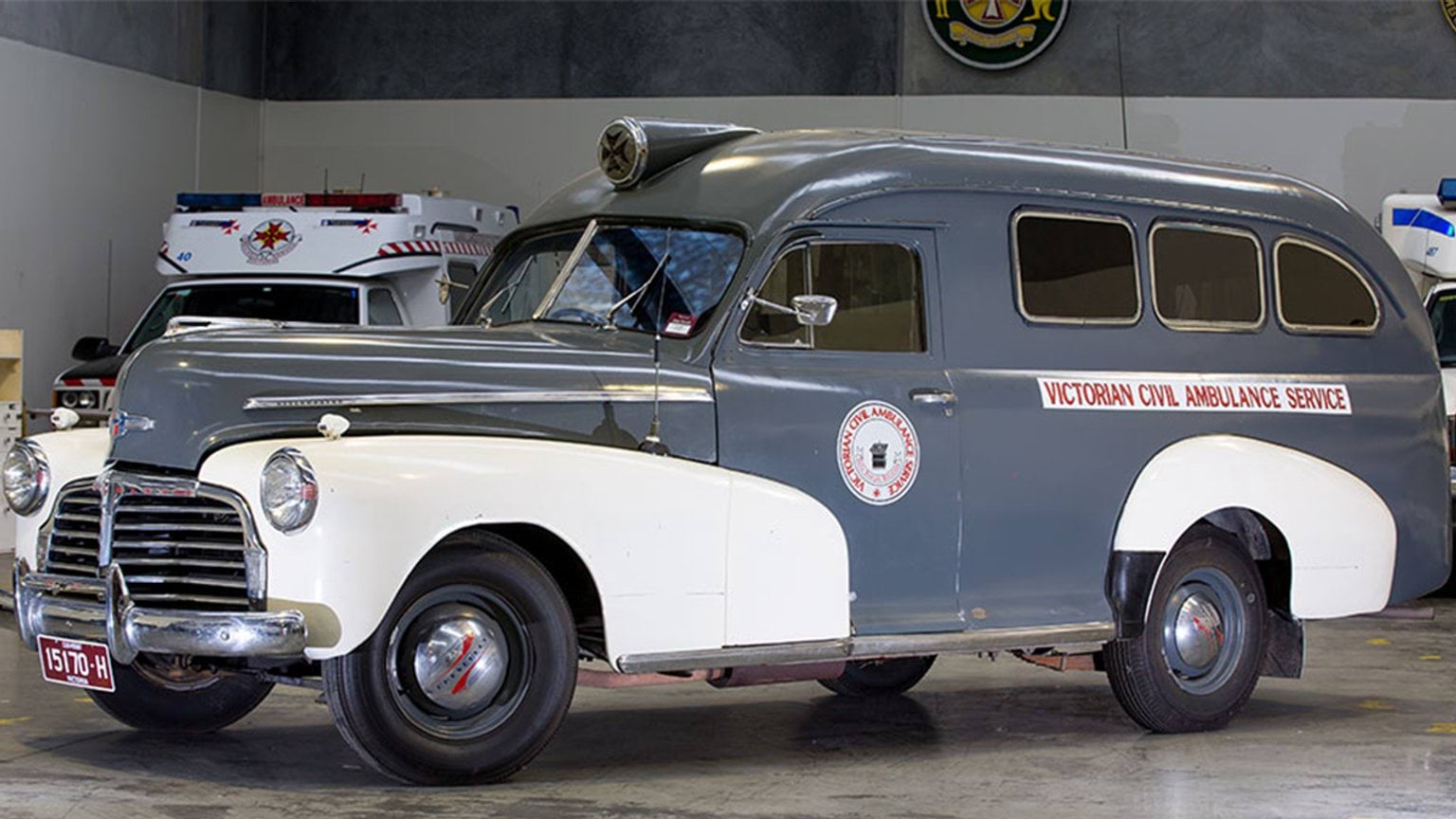A vintage grey and white ambulance parked inside a garage.