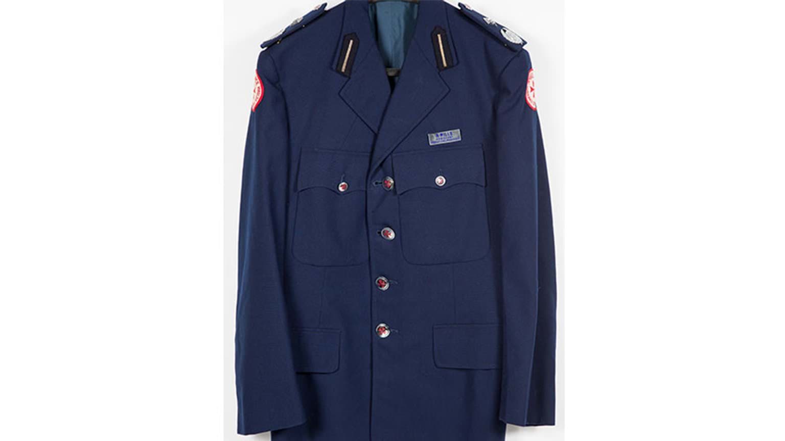 A blue coat featuring gold-red buttons and and a name tag above the front pocket.