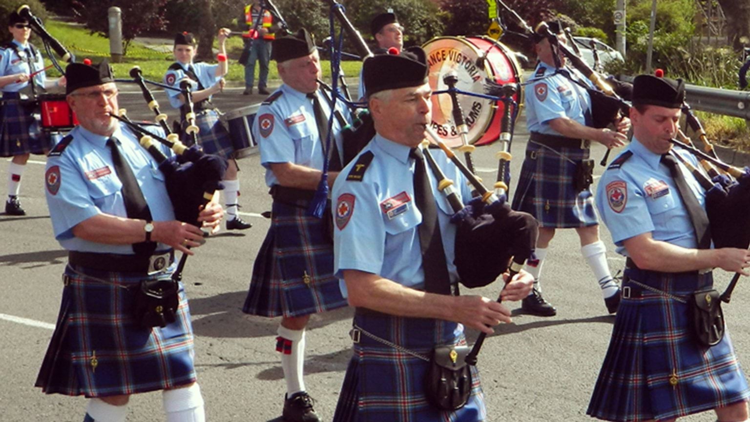 Band members blowing bagpipes as they march down the street.