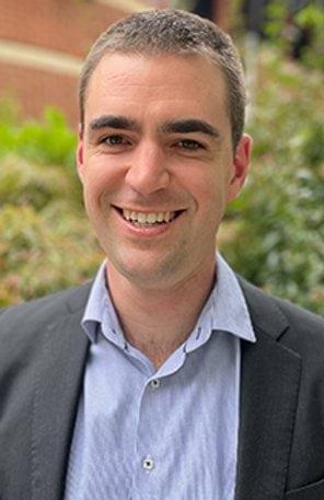 A man in a shirt and suit jacket smiles at the camera
