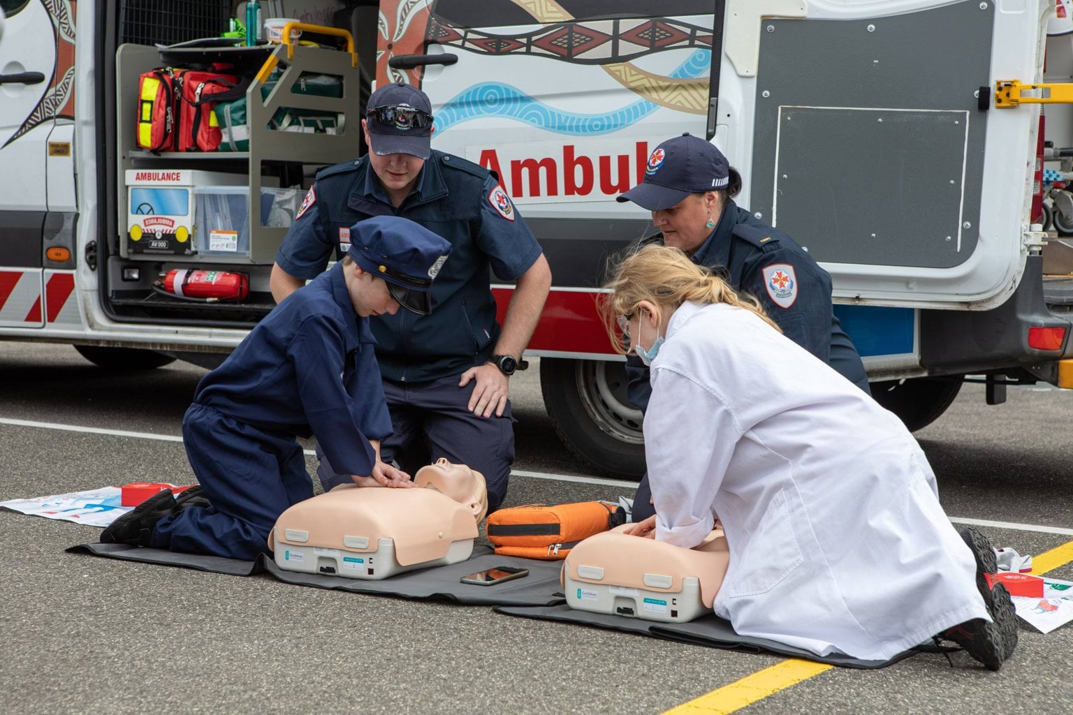 Two paramedics teaching two young children how to perform CPR.