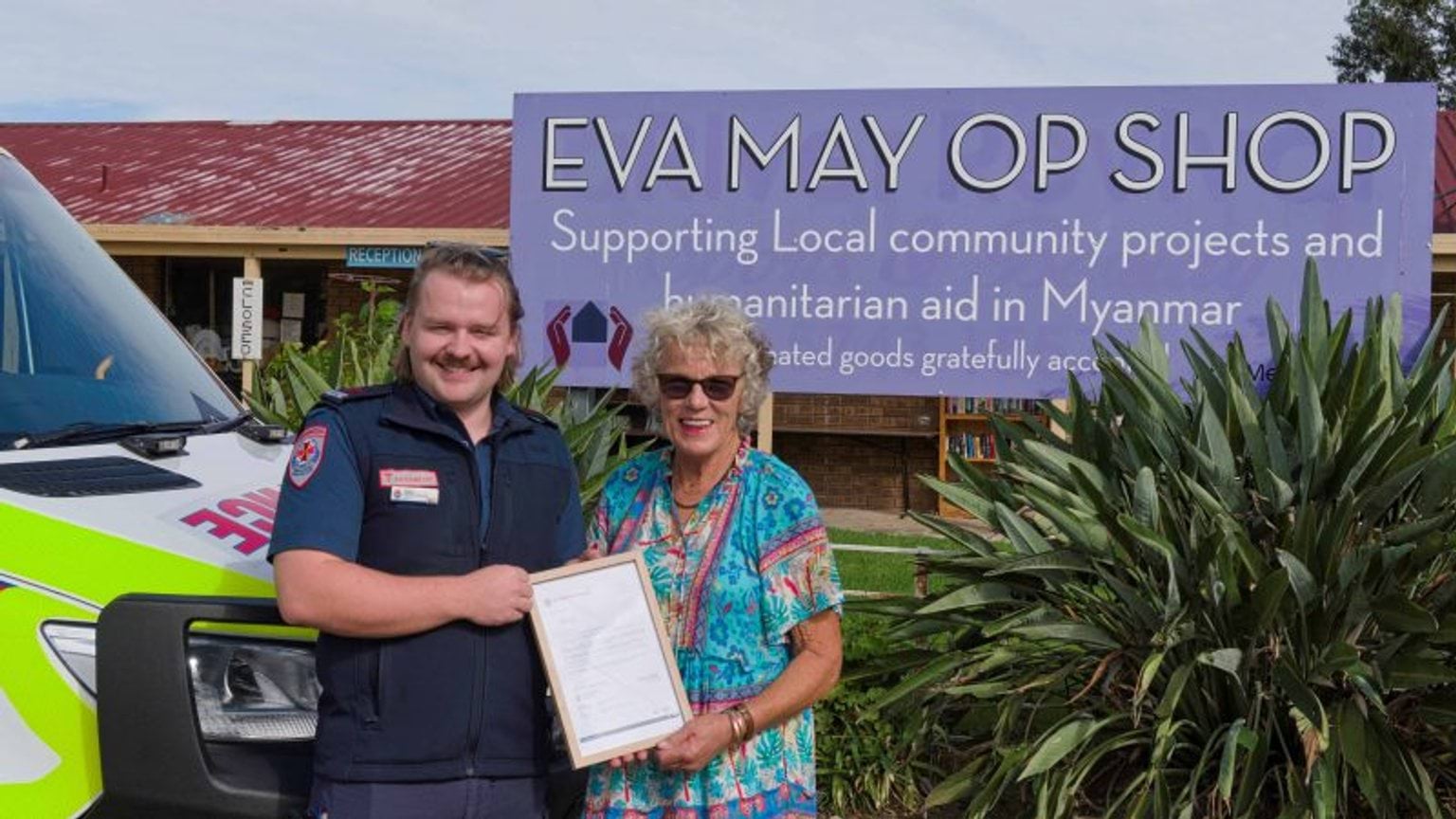A man and woman holding a certificate in front of a sign.