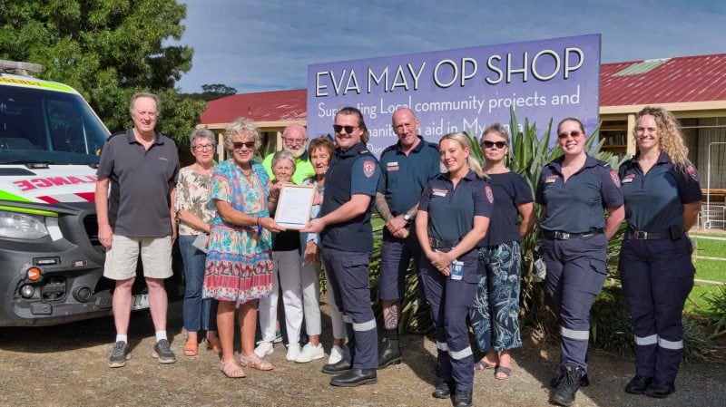 A group of people in front of an ambulance and op shop. 