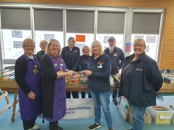 A group of women and one man standing around a table covered in books. 