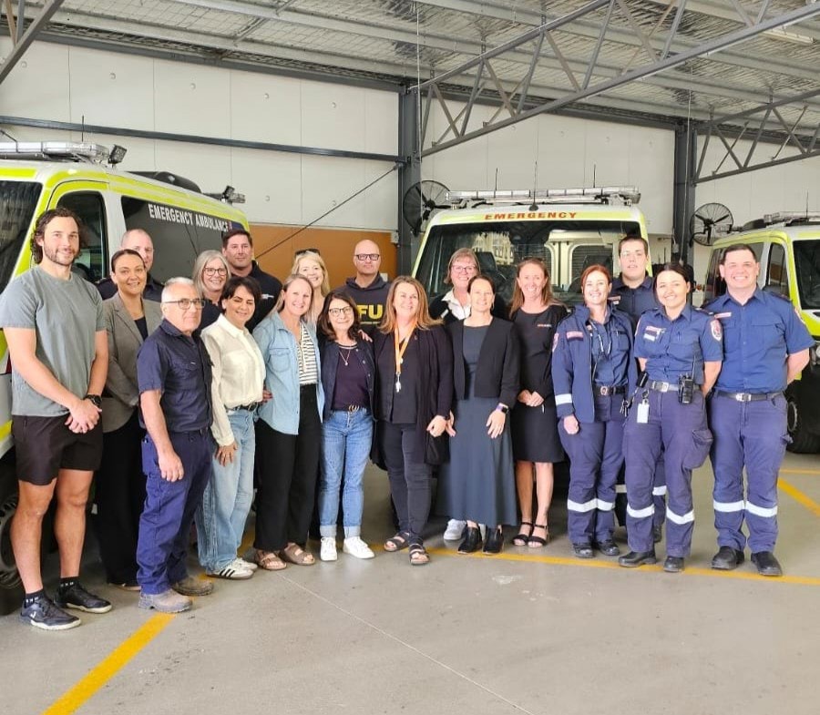 A big group of people smile for the camera in front of ambulances.
