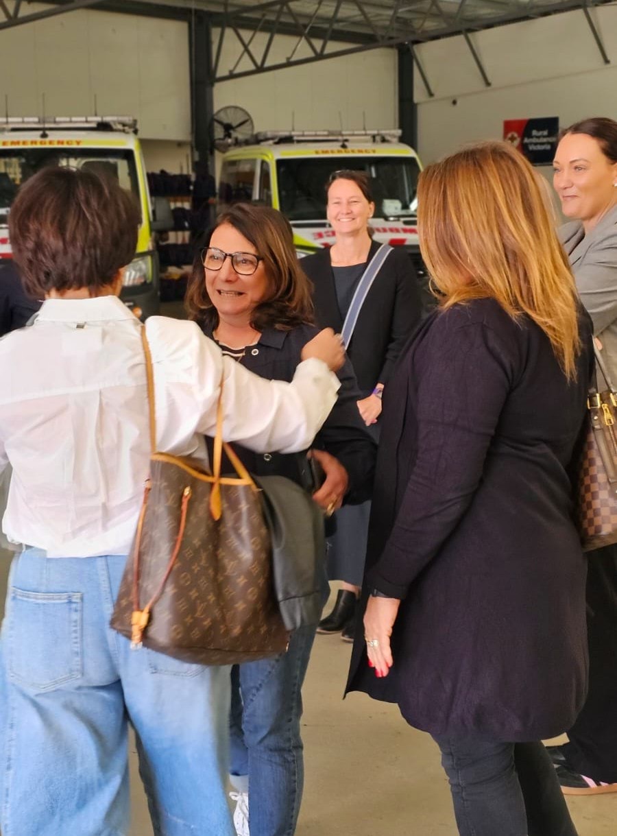 A woman approaches two other women for a hug.