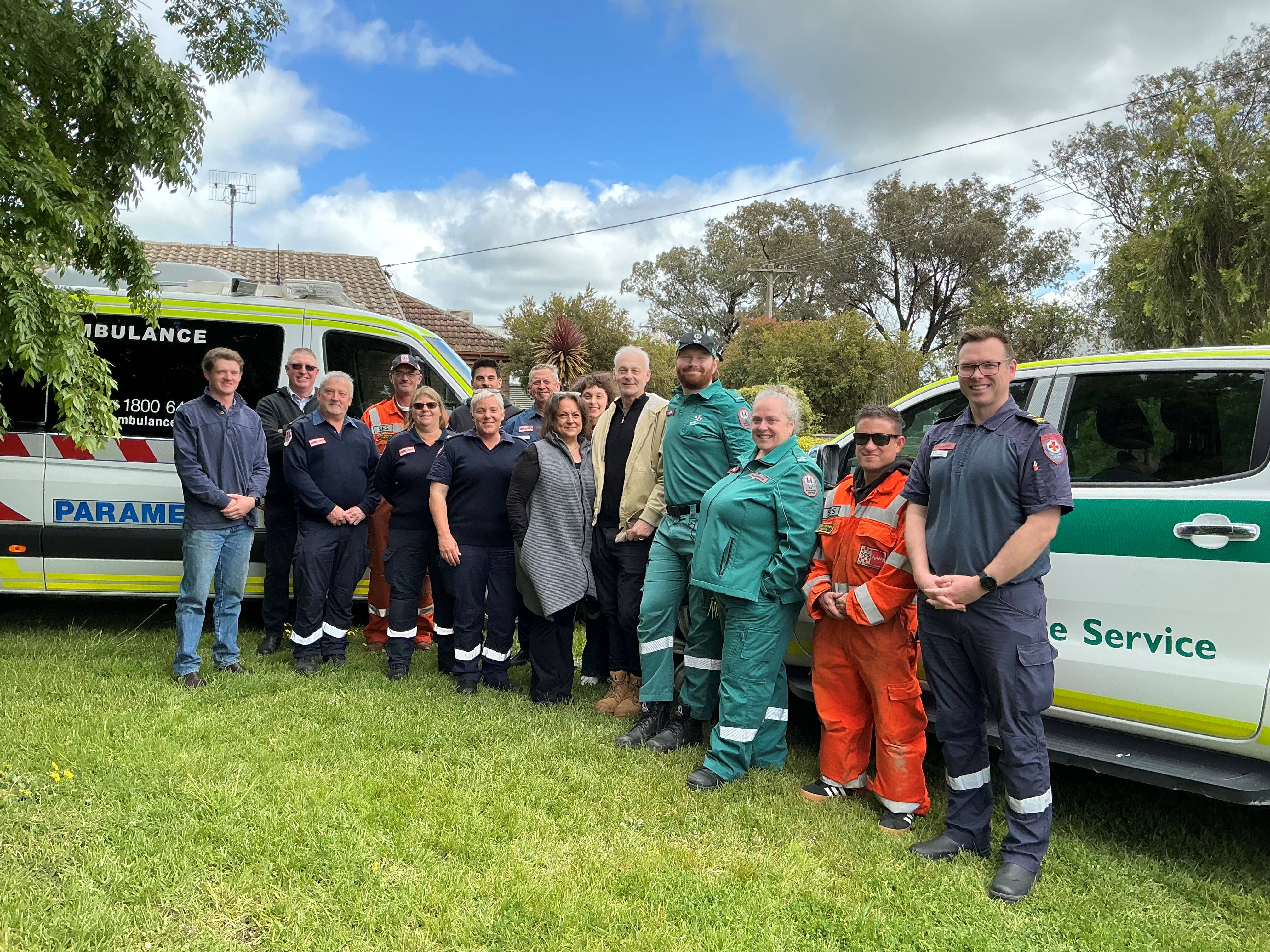 A group of people smile for the camera - some in emergency services uniform. They stand in from of Victorian and South Australian ambulance vehicles.