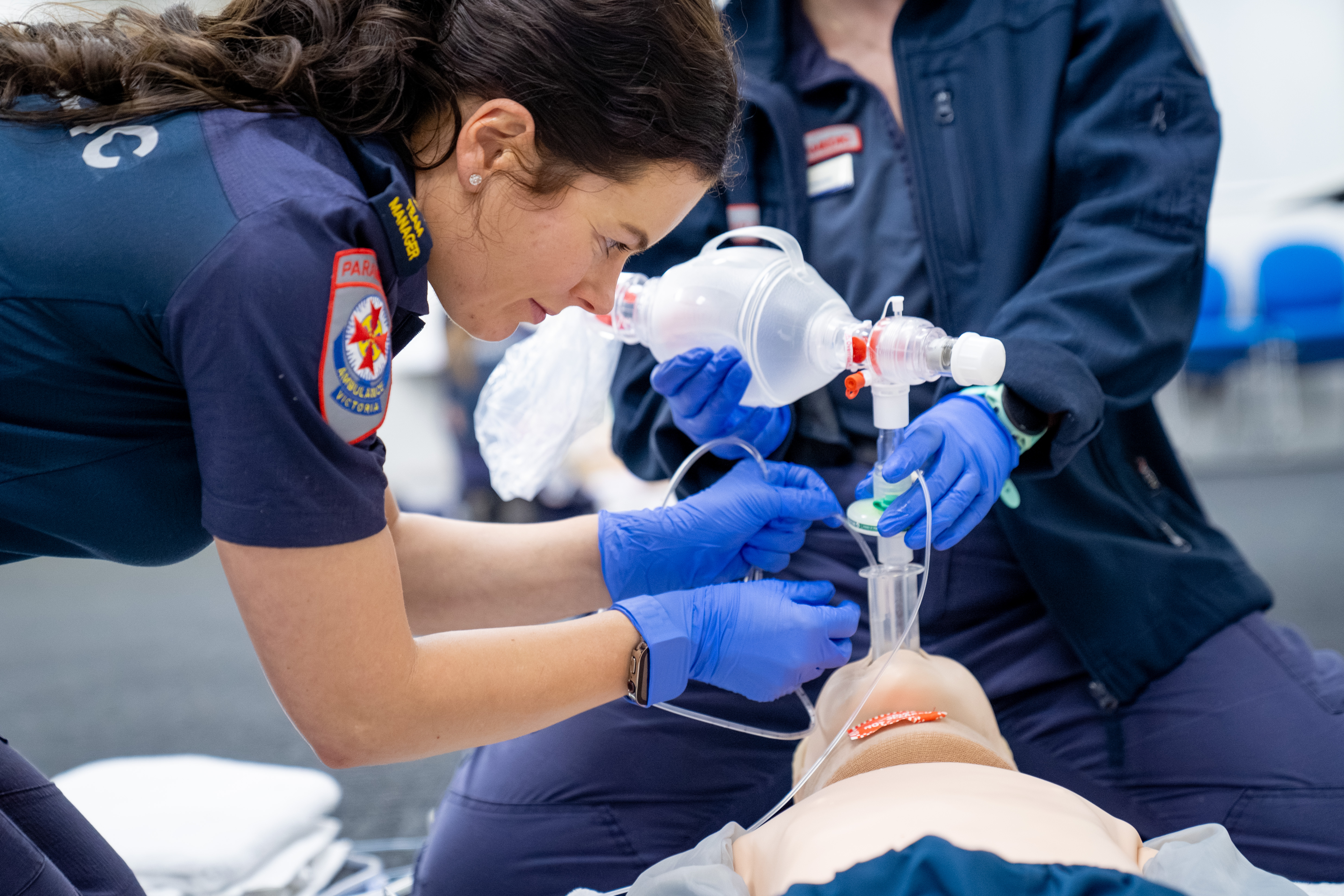 A female paramedic feeding a tube into the mouth of a manikin.